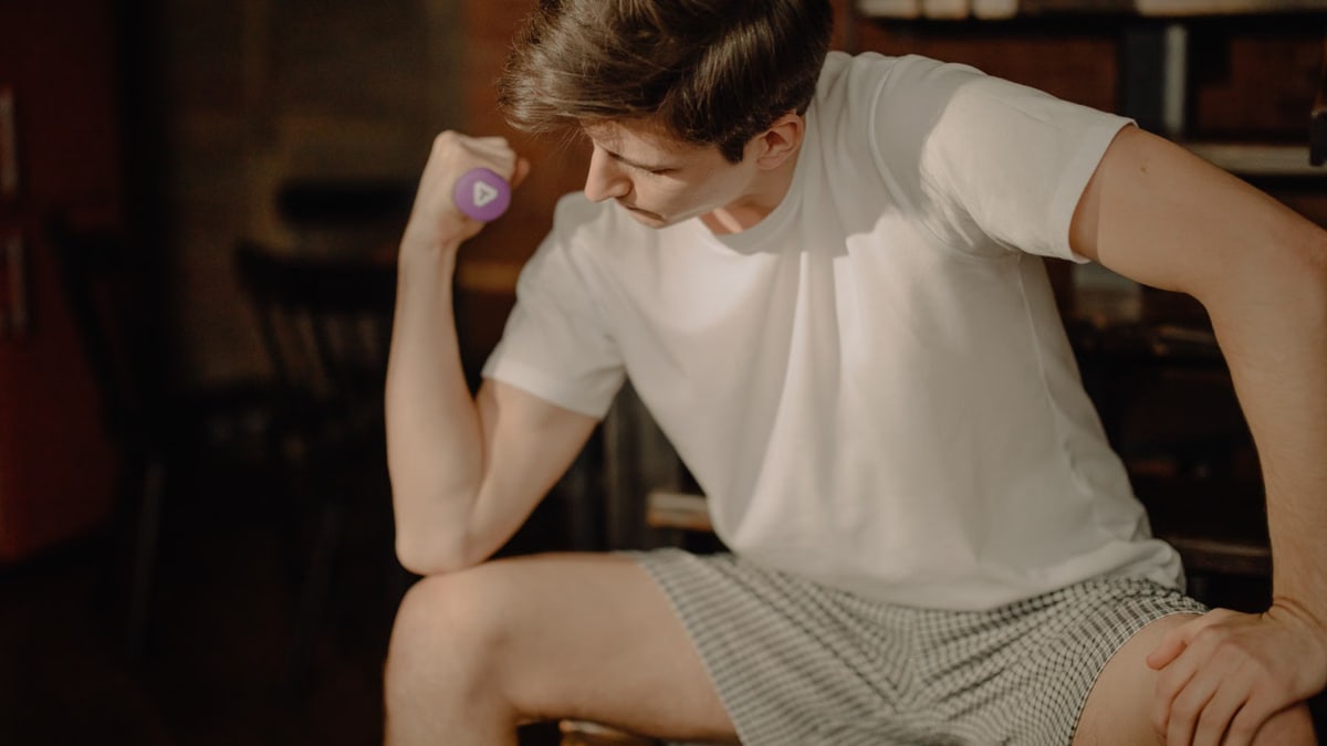 Man in white t-shirt lifting a dumbbell indoors, focusing on fitness.